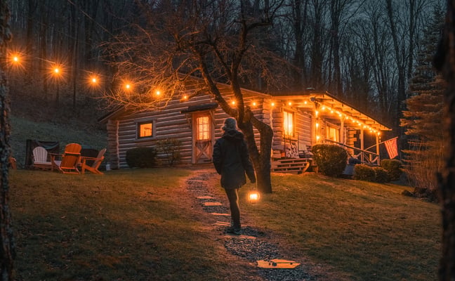 Log cabin with covered porch and Adirondack chairs, surrounded by autumn forest